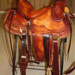 Rancher - dark straight-back, stirrup leathers out and dar, 2-tone, latigo, 2 in bell stirrups, corner bskt wv, barbed wire w rope and scallop border, floral