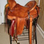 Trainer - fully-tooled basket weave, Santa Fe Diamond with Scallop border, cheyenne roll, latigo wrap, stirrup leathers out, brass oxbows, floral conchos, breeching rings