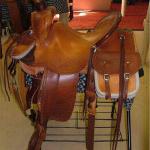 Trainer - dark straight-back, latigo, bags, pouch, star conchos, corner bskt wv, barbed wire w channels, hoof pick case, oxbows, breaststrap, latigo